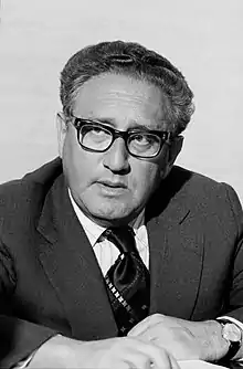 A head-and-shoulders photograph, in grayscale, of Henry Kissinger, looking to the viewer's left with a thoughtful expression on his face.