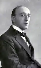 middle-aged white man, clean-shaven, with dark, receding hair, dressed in a suit and bowtie