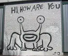 An outline of the frog on the cover of Hi, How Are You? painted on a white wall with the words "Hi, How Are You" above it