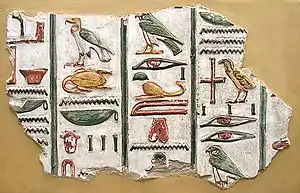 A stone fragment with brightly painted colors and raised-relief images of Egyptian hieroglyphs, written in vertical columns, set against a beige background