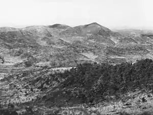 A series of ridgelines and steep hills in the distance, with Maryang-san on the right. In the foreground is a heavily vegetated knoll, with a valley in the intervening ground.