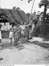 The hoisting of the Raj of Sarawak flag on the civilian compound of the Kuching POW and internment camp on 12 September 1945 by Mr. D. R. Lascelles, the former District Officer for Miri and Mr J. B. Archer, the Chief of Section of Sarawak Civil Service, ex-internees of the Japanese shortly after the surrender of Japan.