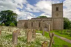 A long stone church in a graveyard, see from the northeast, with a north vestry, and a tower at the far end