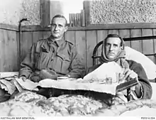 Hugo Thrussel, lying in bed with scarf wrapped around his head, sitting to the side of the bed is his brother Ric Thurssel, in a military uniform with seargent's stripes on his upper sleeve