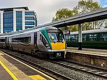 A green Irish Rail Class 22000 at a train station.