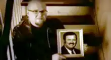 Sitting on stairs, Bart Millard holds up a picture frame of his father Arthur