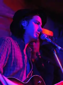 Close up of a man on stage with guitar at a microphone bathed in red and purple low level lighting