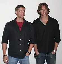 Two men wearing jeans and black shirts.