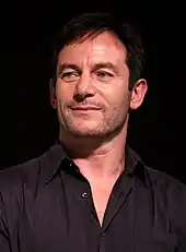 A man with short black hair and a black shirt, who is smiling.