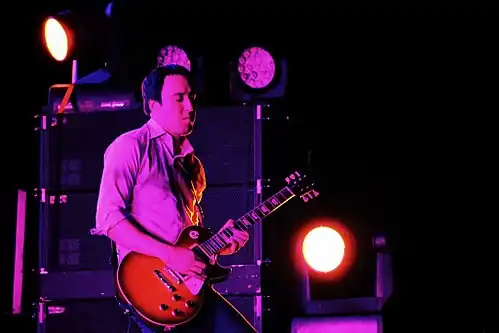 Jeff Schroeder backlit in pink, playing guitar onstage