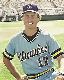 A man in a powder blue baseball jersey with "Milwaukee" written across the chest and a blue cap kneeling on a baseball field