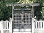 Wooden torii gate and concrete fence in front of trees.