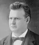 Photographic portrait of a man about forty, with short hair standing straight. He is dressed formally with a bow tie visible, and is facing somewhat to the left.