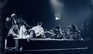 A quartet performs acoustic music to the audience while being covered by a dark stage-light.