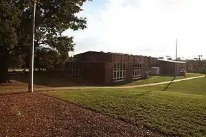 A photo of a walking path on a large field leading to a large, brick building with two floor-to-ceiling windows.