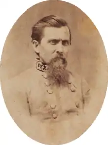 Sepia tone photo shows a frowning man with a beard and dark combed-back hair. He wears a gray uniform with three general's stars on the collar.