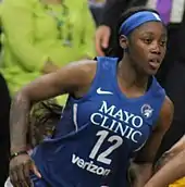 Waist high portrait of young woman running to the right wearing navy basketball uniform and blue headband