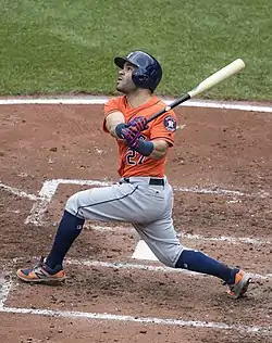 A man in an orange baseball uniform and dark blue batting helmet swings his bat.