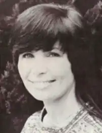 A young white woman with short dark hair styled in long side-swept bangs; she has striking light-colored eyes