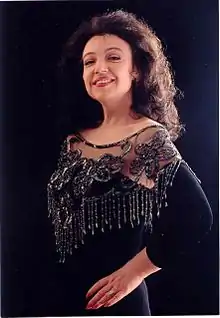 A photograph of a smiling white woman with long dark wavy hair, posing in an elegant black evening dress