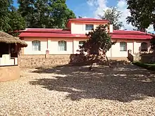 Photograph of the house with the driveway and a smaller outhouse visible