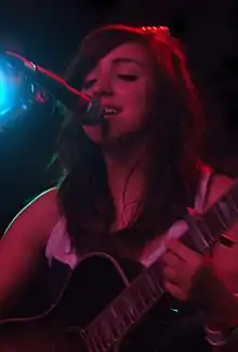 Kate McGill singing into a microphone and playing guitar onstage