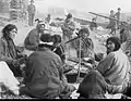 Group of Kets around a campfire. The people in the background wearing fur hats are Russians.