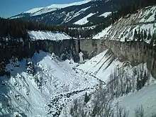 View of a waterfall dropping from a cliff in a basin-like depression in a mountainous landscape.