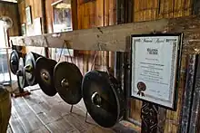 Six black hanging gongs with golden knobs in a room made of bamboo. In the image's right (forefront) is a certificate from the Malaysia Book of Records.