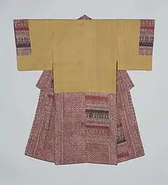 A man's underkimono viewed from the back. It has short sleeves sewn to the body for most of their length. The underkimono is made of a light yellow fabric with fine beige stripes, and the hems and collar are made from two different kinds of arabesque fabric on brick red and darker red.