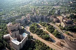 Freedom Square, Kharkiv in 2003, showing half of the square area (only the circular neighbouring park on the north-western edge). The square proper begins at the large statue of Lenin (this statue has since been removed). This statue of Lenin is seen in the lower right corner, casting a long shadow which points into the square.