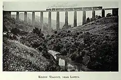 A black and white image of a steam train crossing a tall viaduct