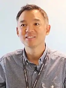 Portrait photograph of Kim smiling, while wearing a black lanyard.