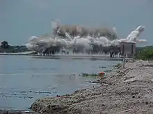 A color photograph of a large cement structure on the C-38 Canal being destroyed with explosives