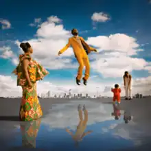 A Black man in a yellow suit levitating above a puddle on the gray ground.