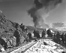 Soldiers watch a hill in front of them as aircraft drop bombs on it