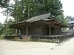 Wooden building with a hip-and-gable roof and step canopy. A shorter aisle is attached to the right side.