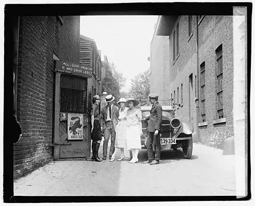 Gerswhin's work has been cited by writers and scholars as embodying the Jazz Age's zeitgeist with its flappers and speakeasies. Above: Patrons and a flapper await the opening of a speakeasy in 1921.