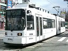 A white light rail vehicle approaches a crosswalk