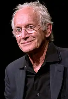 A white-haired man in a tuxedo looks off to one side, smiling.