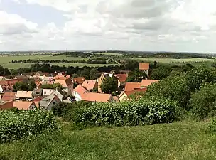 Low hills, barely higher than the church's steeple, surround a village.