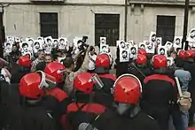 Demonstrators holding pictures in front of uniformed people in red helmets, perhaps police officers