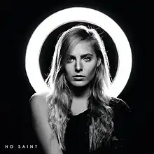 A black and white image of a woman wearing a black top and posing in front of a circular light.