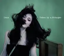 Shot of Lena wearing a black dress and a white neckless. Information on the song is placed on her left and right.