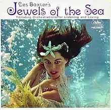 Cover image for Jewels of the Sea. There is a white band with text above a photograph. On the white, mid-size black text says "Les Baxter's". Directly underneath, larger purple text says "Jewels of the Sea". Under that, small black text says "Titillating Orchestrations for Listening and Loving". The photograph depicts a Caucasian woman with brown hair from the waist up, posing underwater among bubbles and kelp strands. Her hair floats in the water. She is apparently nude but her chest is hidden by her crossed arms and some strategically placed kelp. She has glamorous makeup and large pieces of silver jewellery in her hair and around her neck.