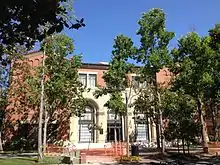 An exterior shot of a red brick building behind several trees.