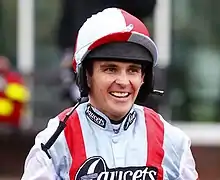 Headshot of a man in white and red horse racing kit