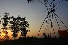 A picture of a swing made from four bamboo plants, during dawn time