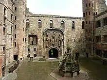 A red stone courtyard with a doorway in the middle background and an ornate fountain in the mid-ground.