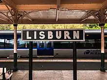 A retro-style sign reading 'Lisburn' on a platform at Lisburn railway station.